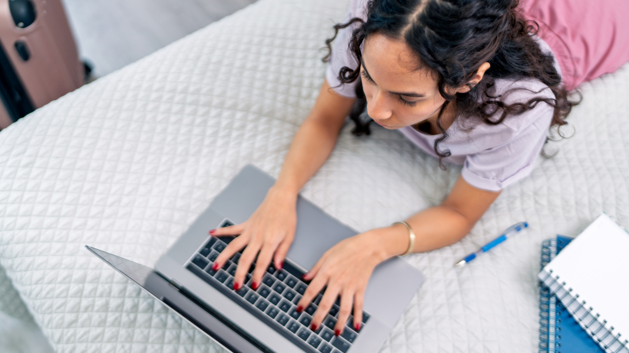 Airbnb guest working on a laptop while lying on a bed with luggage nearby, illustrating modern guest behavior and expectations for seamless digital communication during a stay