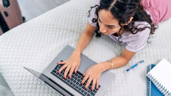 Airbnb guest working on a laptop while lying on a bed with luggage nearby, illustrating modern guest behavior and expectations for seamless digital communication during a stay