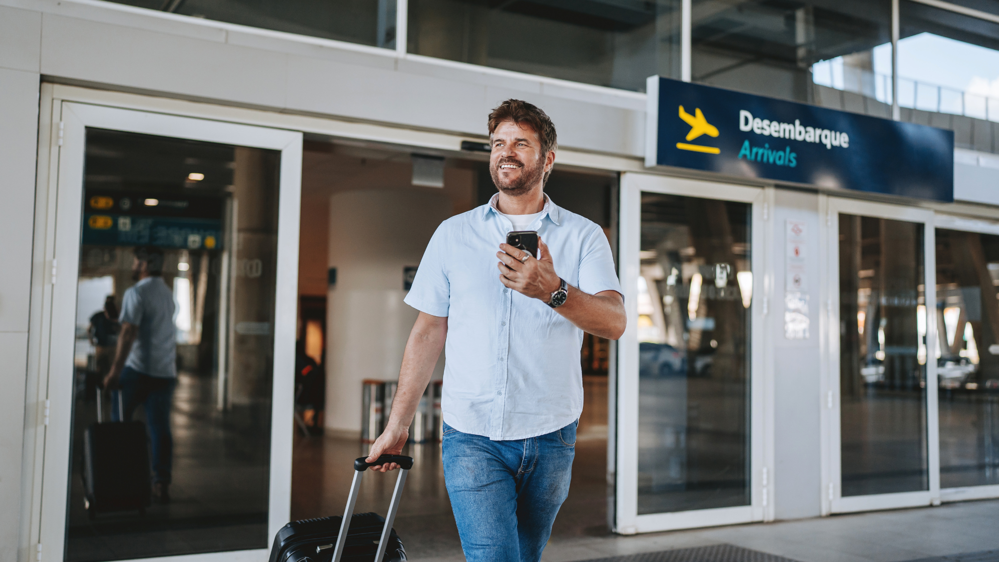 Traveler walking out of an airport arrivals entrance with a suitcase, checking a phone—ideal visual for an airport pickup upsell.