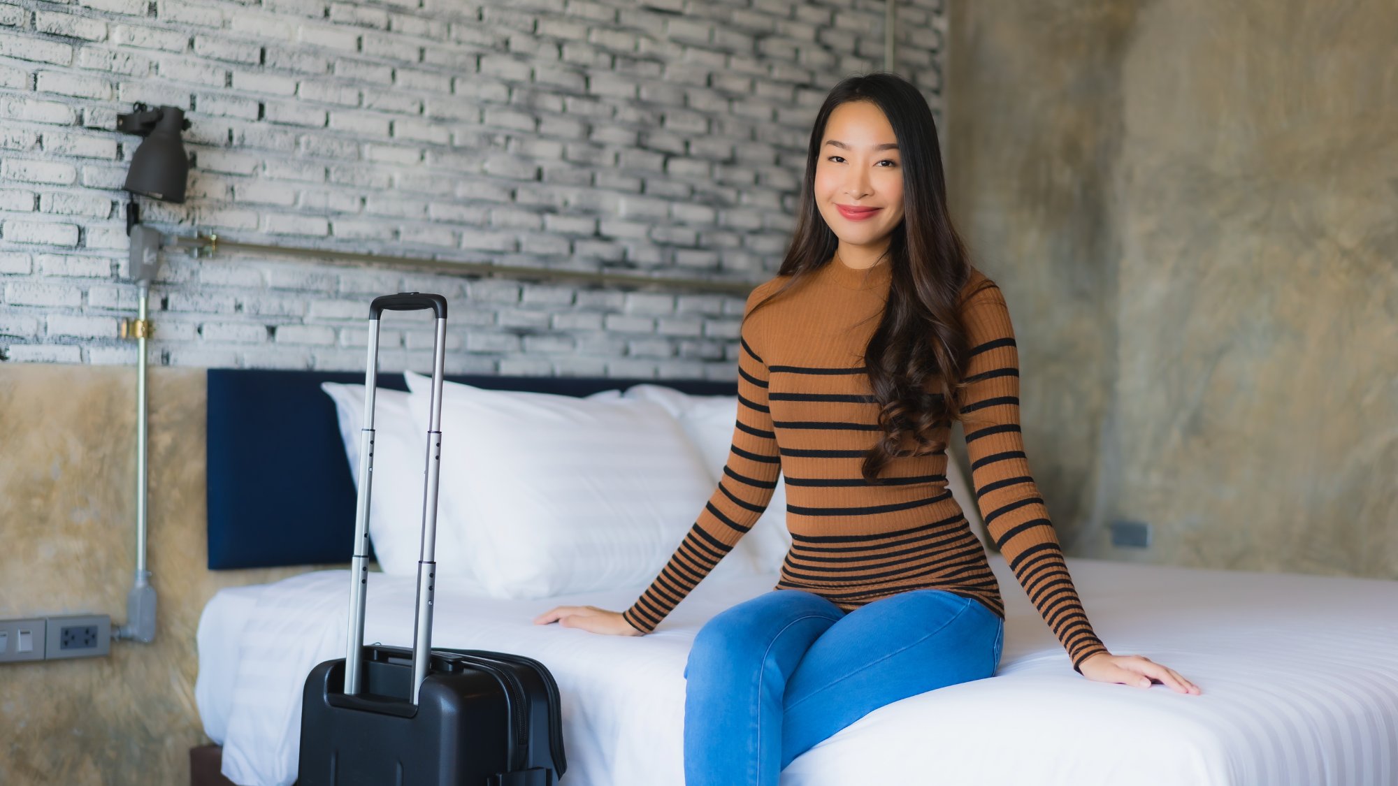 Guest sitting on a hotel bed with a suitcase in a modern room, representing a mid- or long-stay rental experience.