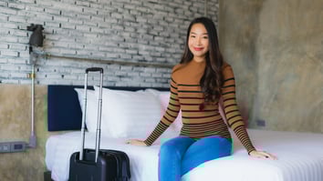 Guest sitting on a hotel bed with a suitcase in a modern room, representing a mid- or long-stay rental experience.