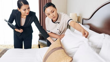 Property manager supervising housekeeping staff while inspecting bed linens during short-term rental turnover to ensure guest-ready cleanliness.