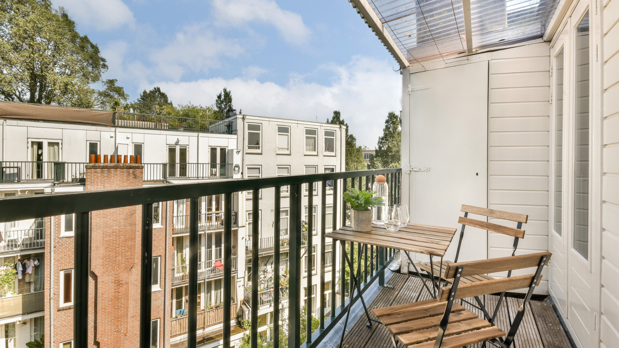 Modern Airbnb apartment balcony with outdoor seating overlooking residential buildings, representing guest experience and short-term rental property quality.