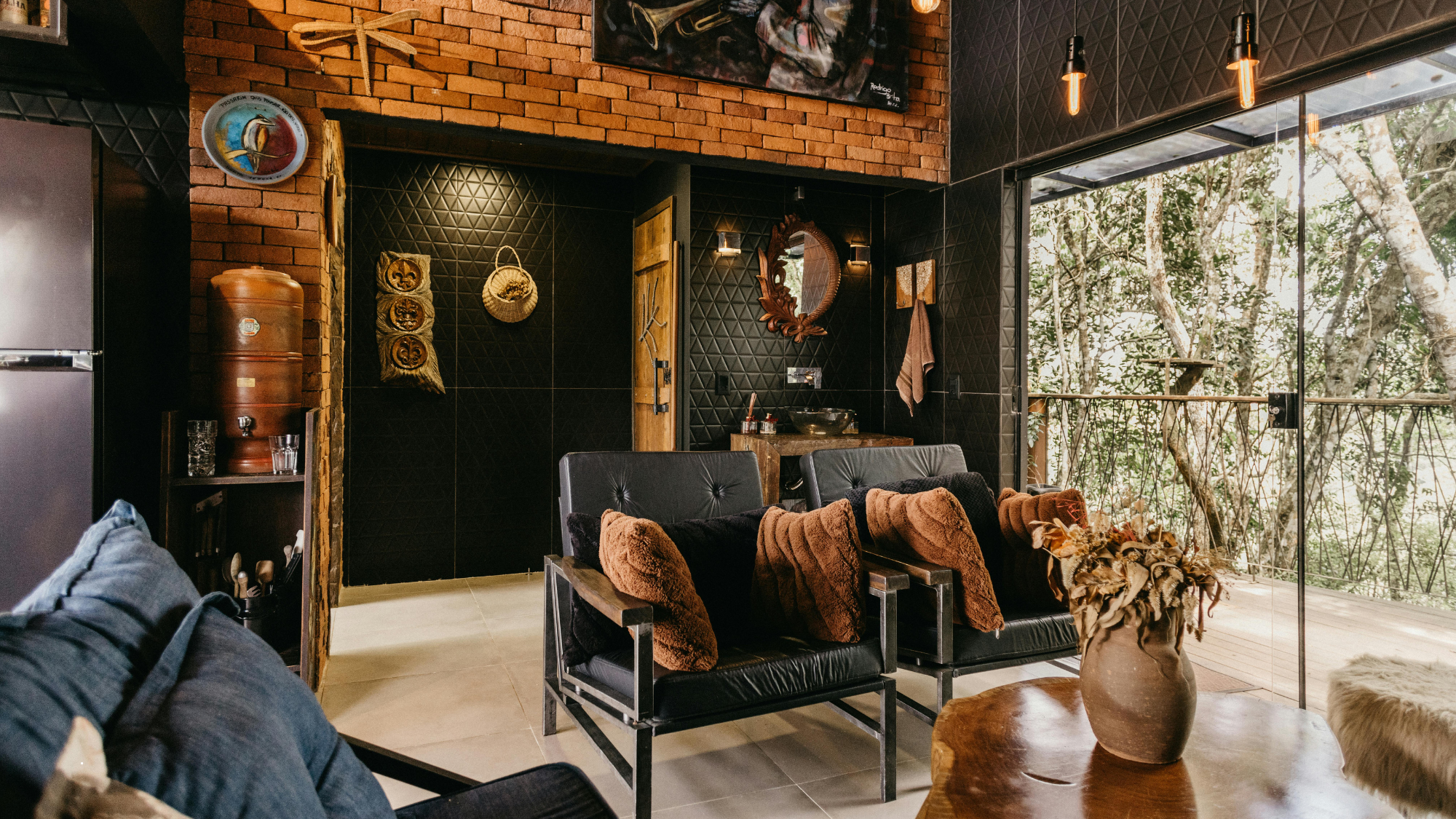 Warm, modern Airbnb living room with leather chairs, brick accents, large windows facing the trees, and cozy décor—representing elevated guest experience.